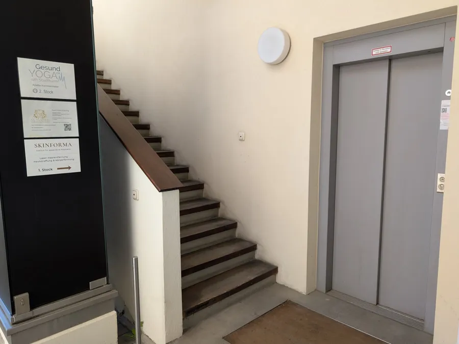 Treppenhaus mit Aufzug und Schild „SKINFORMA – 1. Stock“